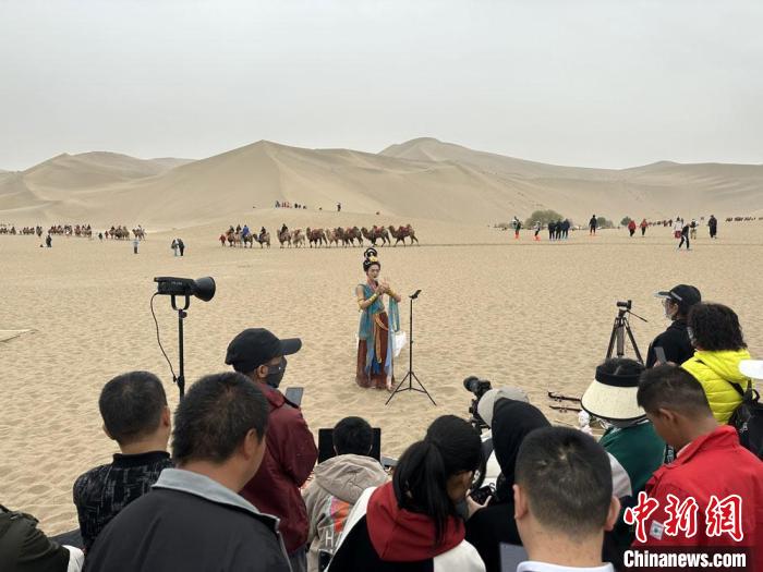 圖為2023年4月底，敦煌大漠“逐舞者”奧楠在鳴沙山月牙泉景區(qū)視頻直播，吸引游人圍觀?！●T志軍 攝